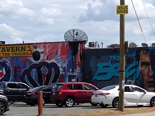 A yellow Jesus Saves sign up on a pole with a graffiti painted wall in the background